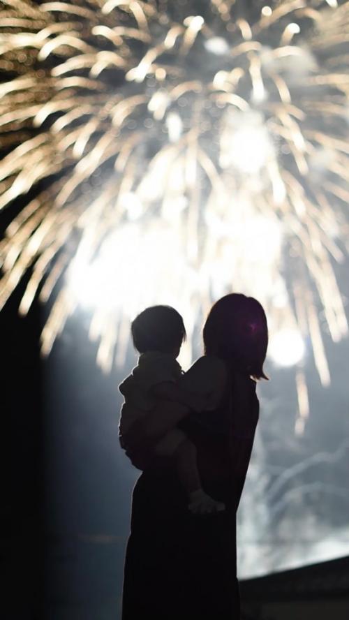 子どもを抱く母親とバックに写る花火の写真